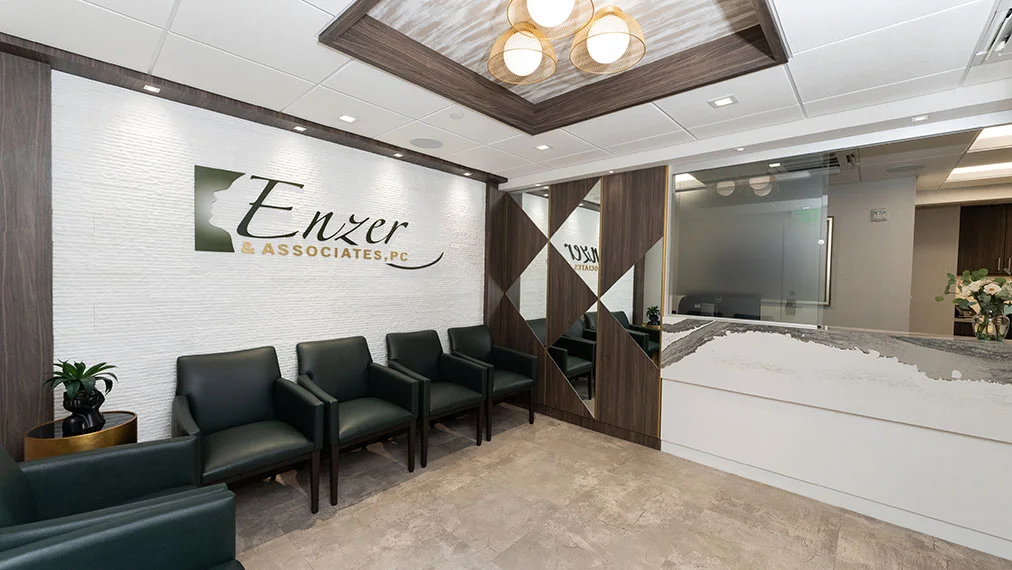 The modern and stylish waiting room of Enzer & Associates, P.C., featuring a textured white wall with the company logo, dark green leather seating, a mirrored wall section, and a white reception desk with a marbled gray pattern.